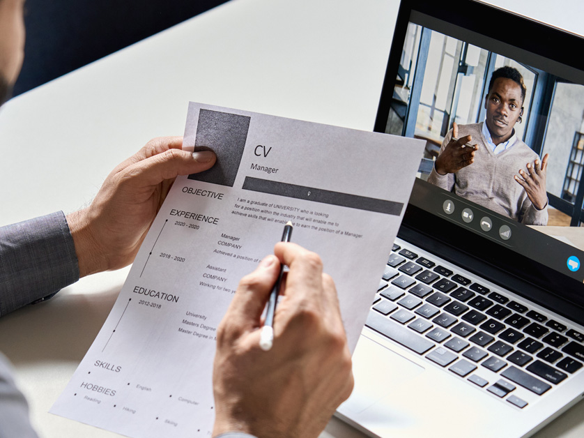 close up of hands holding cv in front of laptop with man on it